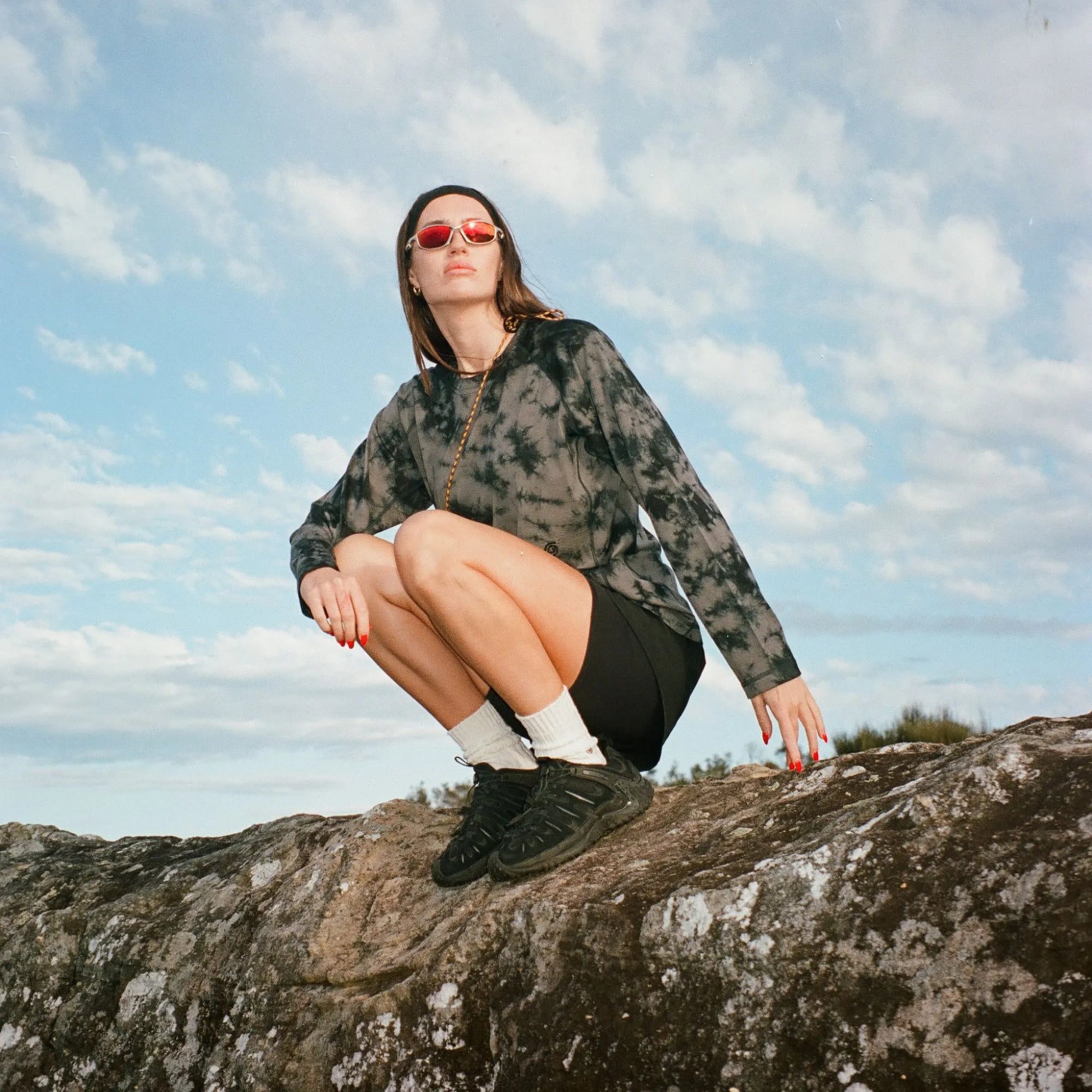 Woman sitting on a rock with a blue sky and clouds in the background