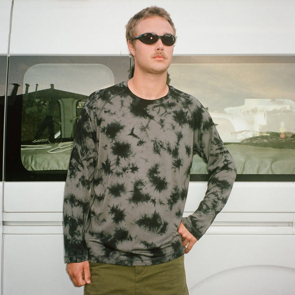 Man wearing a black and gray tie-dye shirt standing in front of a white van.