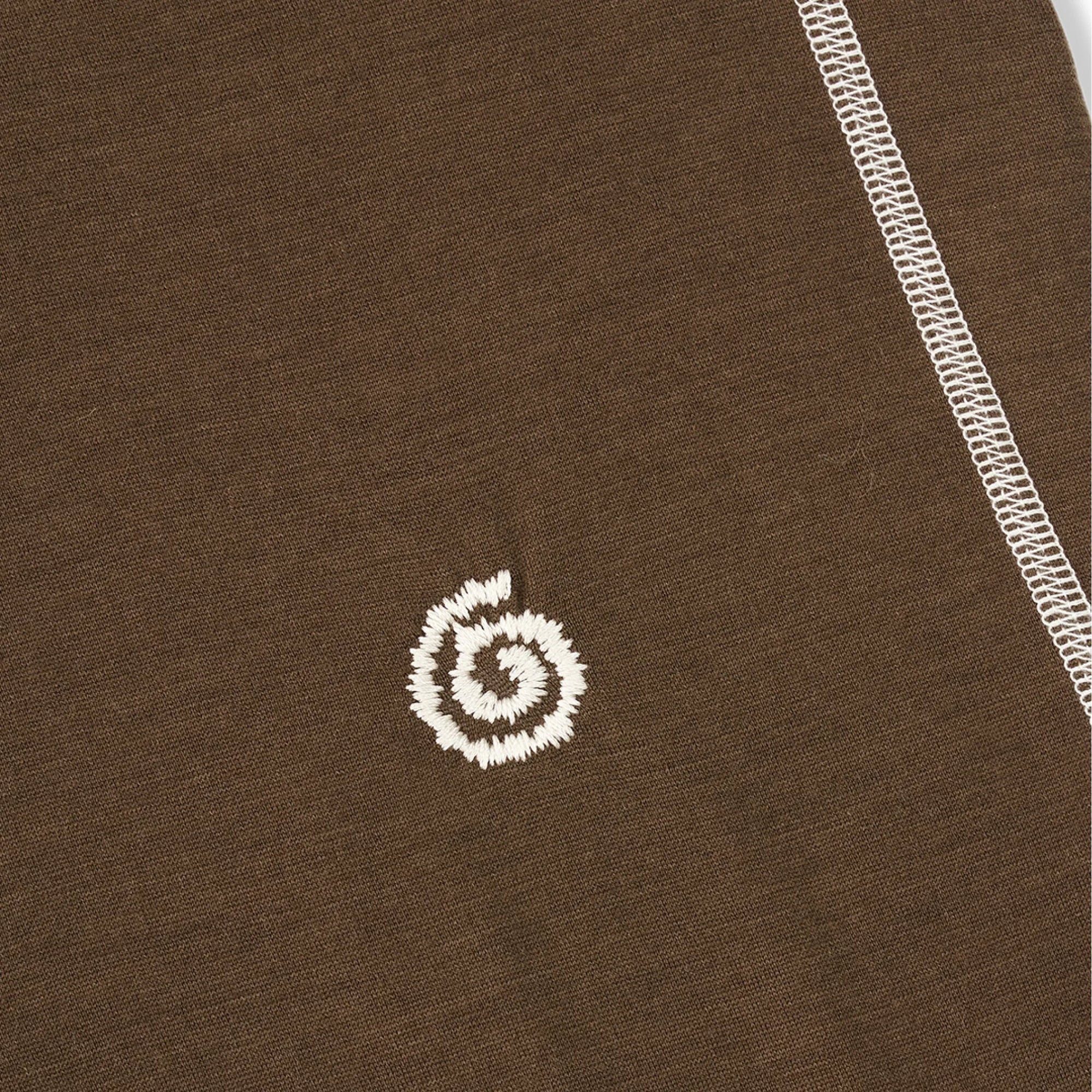 Close-up of a brown fabric with a white embroidered logo on a plain background