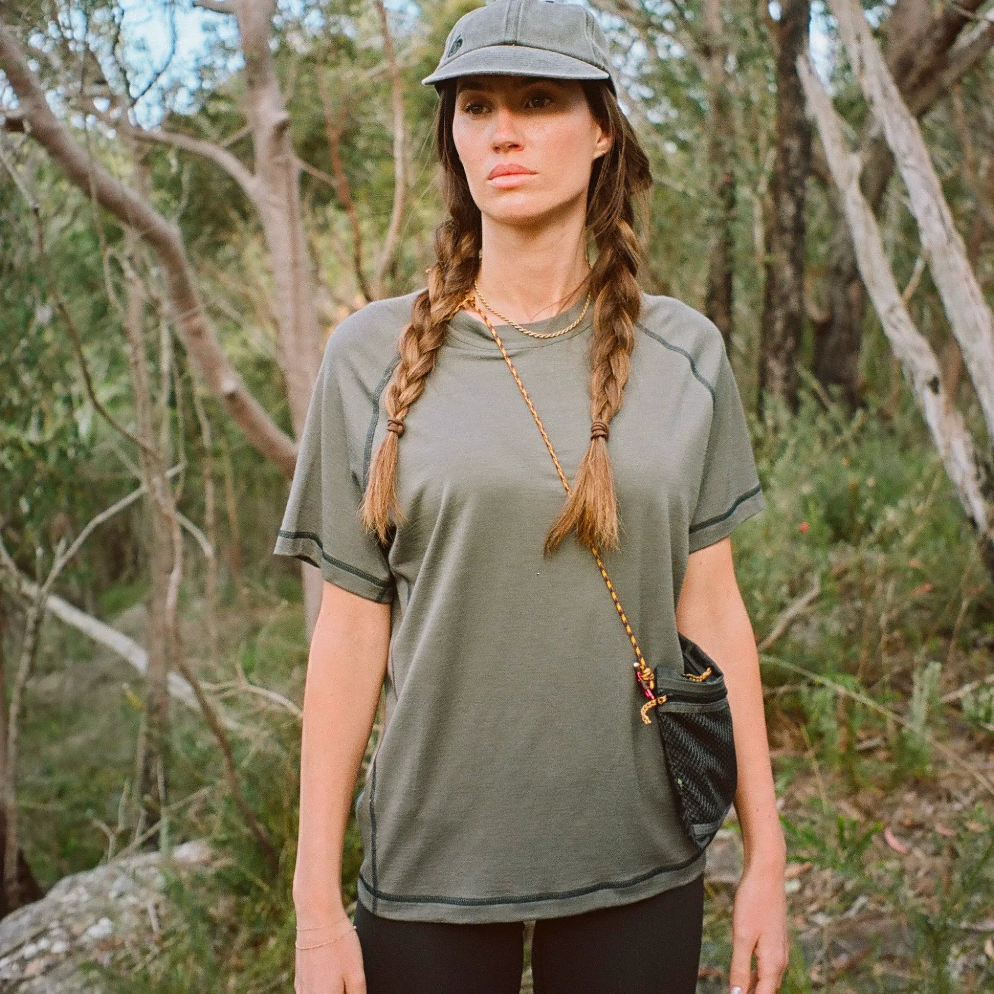 Woman in a gray shirt and cap standing in a forest