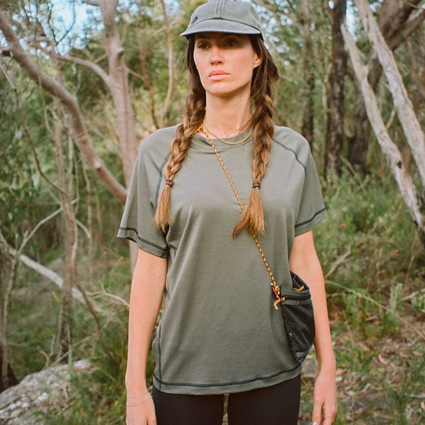 Woman in a gray shirt and cap standing in a forest