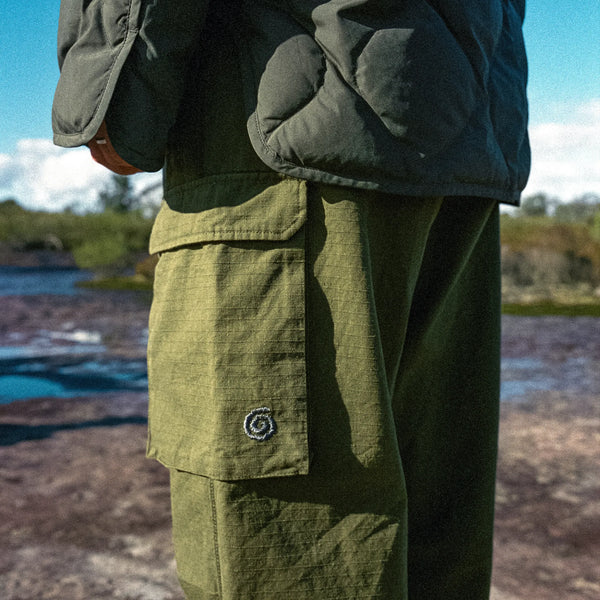 Person wearing green pants with a logo and a dark jacket outdoors.