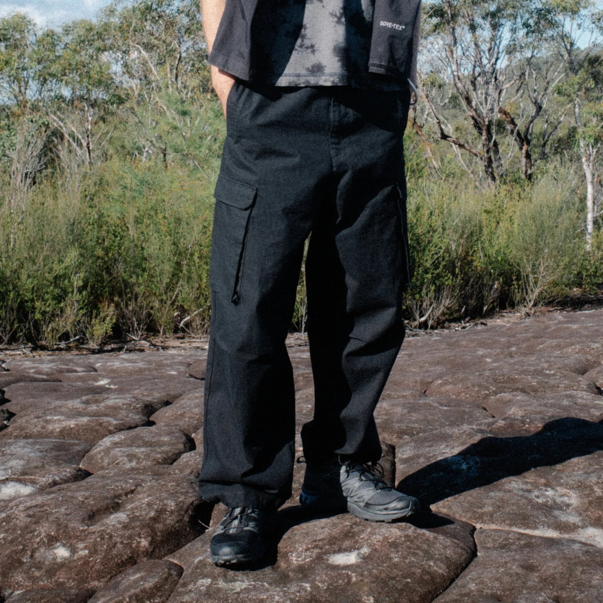 Person wearing black pants and shoes standing on a rocky surface with a natural background