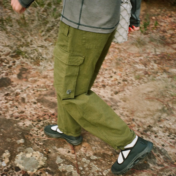 Person wearing green cargo pants and black shoes on a rocky ground