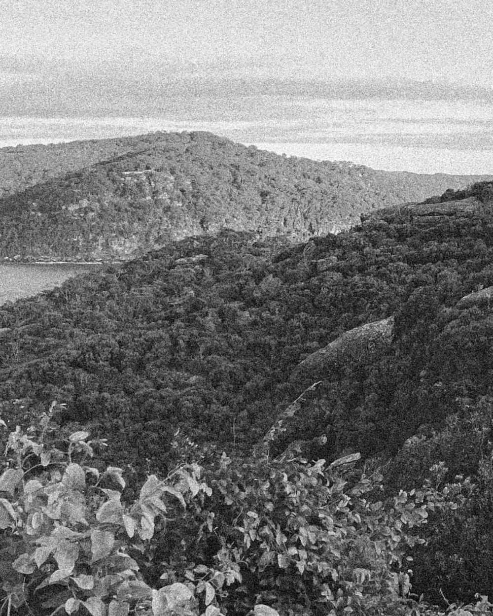 Black and white photograph of a scenic landscape with hills and a body of water.