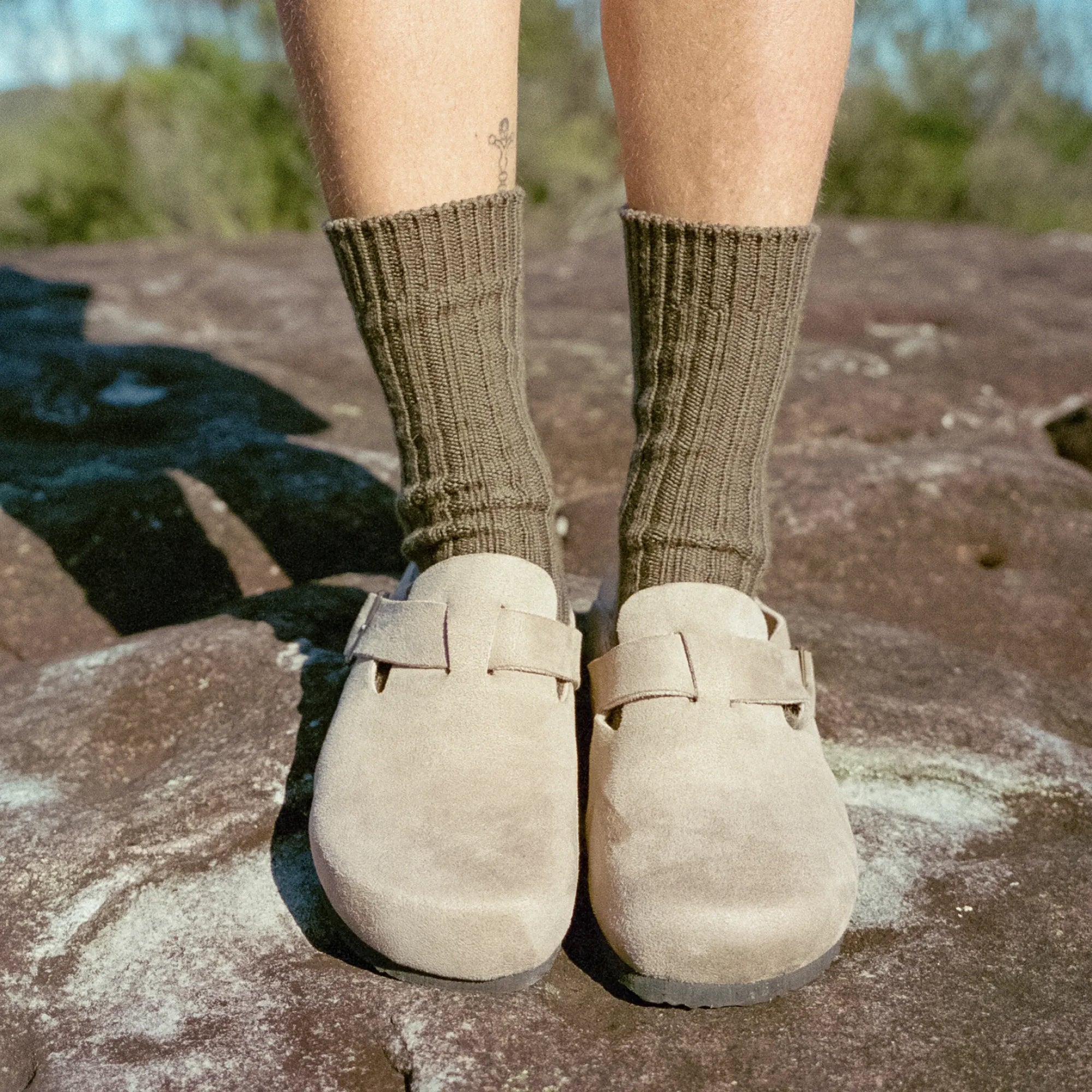 Person wearing brown socks and beige shoes on a rocky surface with a natural background